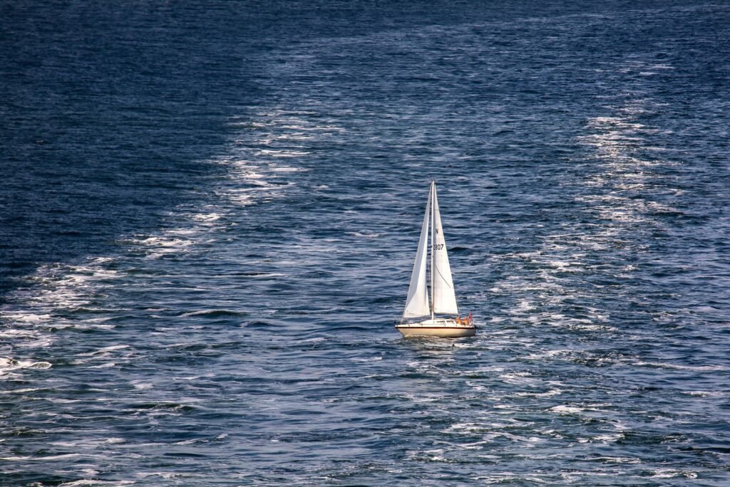 A lone sailboat gliding through the vast open ocean under clear daytime skies