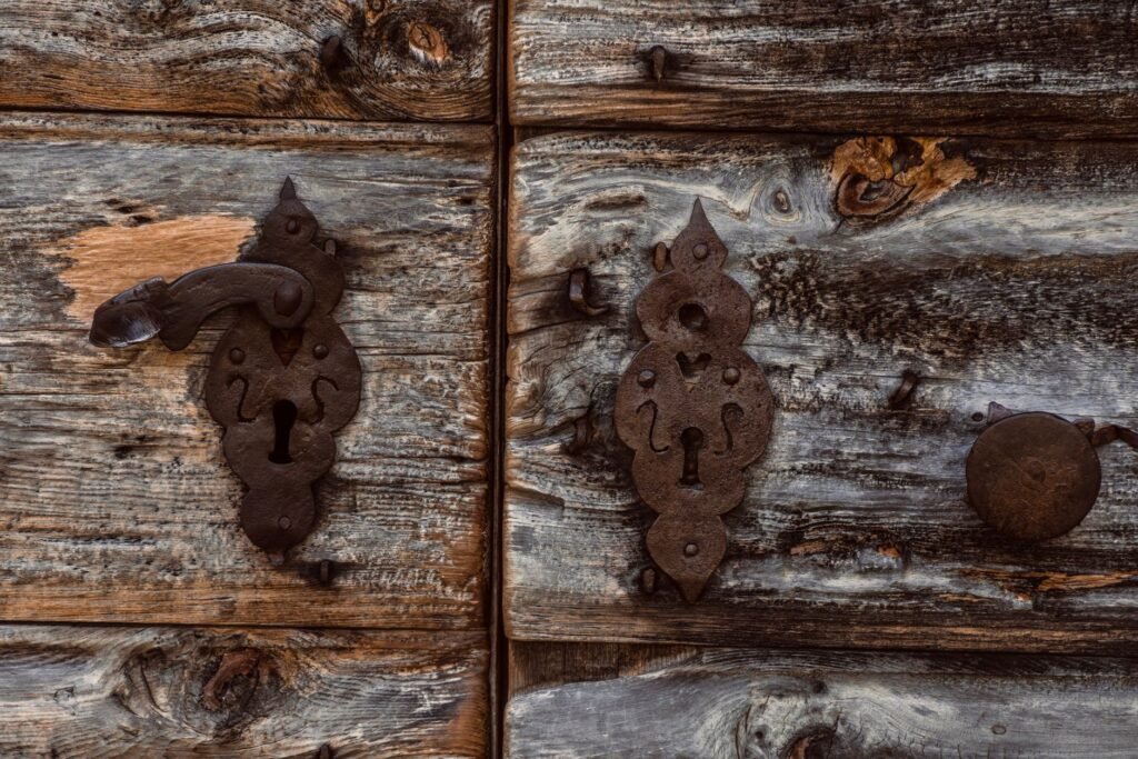 Weathered wooden door with two dark iron lever handles and ornate keyhole plates