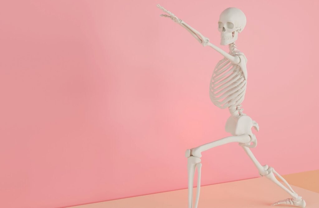 White plastic skeleton model posed in a lunge with one arm raised against a pink wall