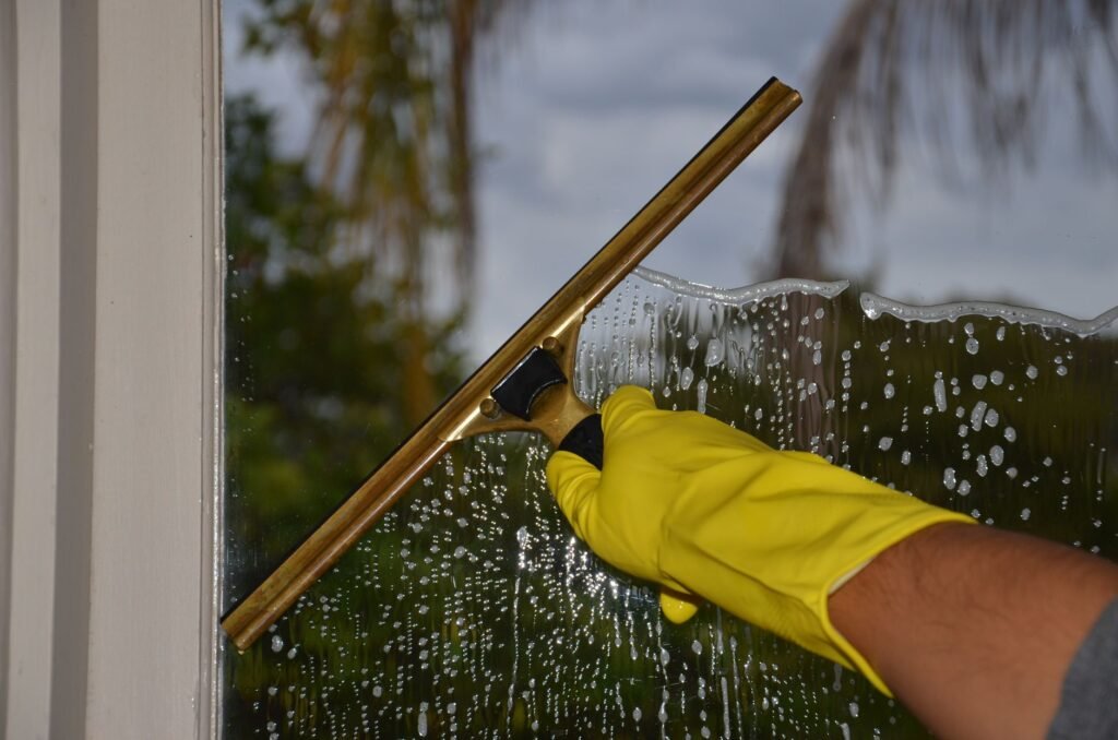 Gloved hand pulling a squeegee across soapy window glass