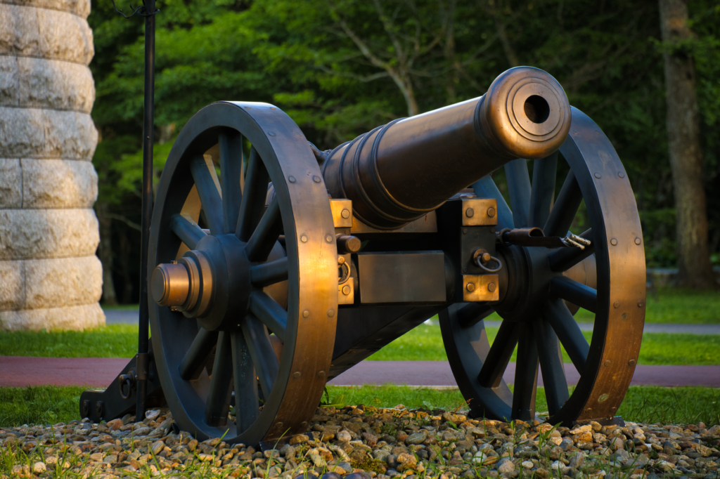 Old cannon with a bronze colored barrel on a spoked wheel carriage set on gravel
