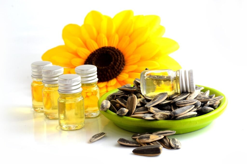 Small glass vials of golden oil beside a yellow sunflower and a green bowl of sunflower seeds