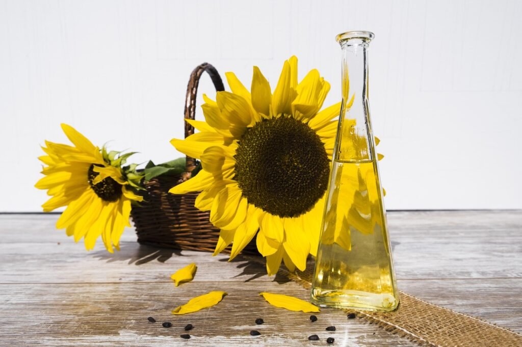 Glass bottle of golden oil beside bright sunflowers in a wicker basket on wood
