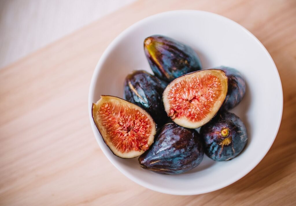 Whole purple figs and halved figs with red centers in a white ceramic bowl