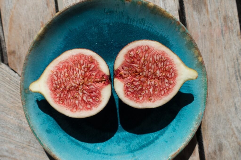 Two halves of a ripe fig showing pink seeded flesh on a teal ceramic plate