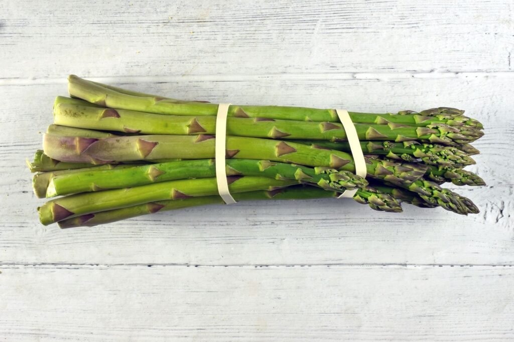 A close-up view of a fresh asparagus bundle on a rustic wooden background, highlighting its vibrant green c...