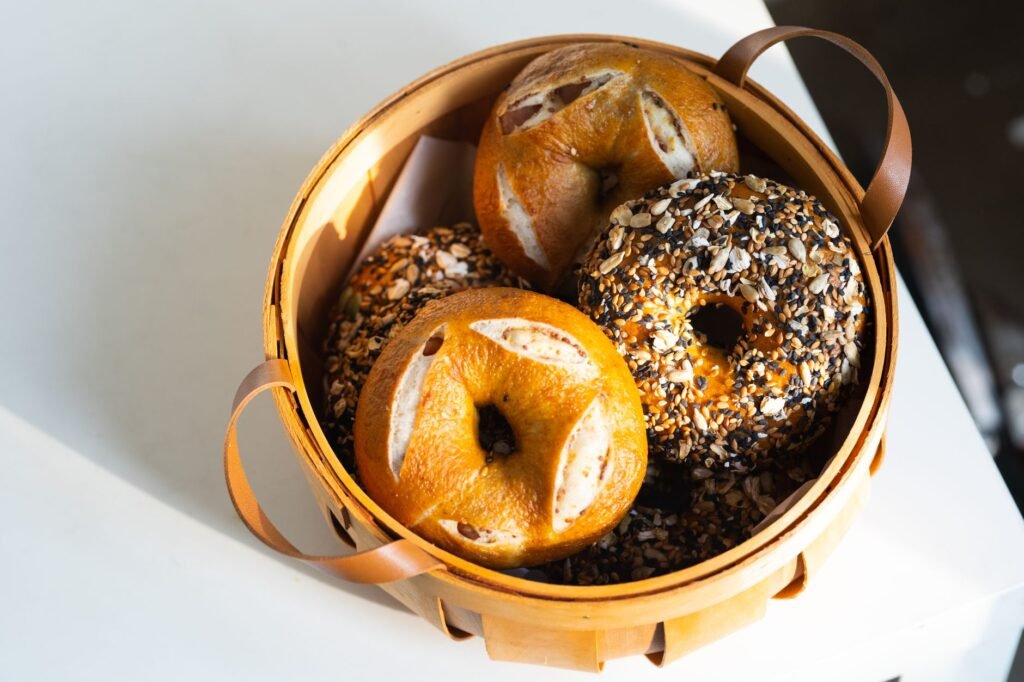 A variety of freshly baked artisan bagels sit charmingly in a wooden basket, highlighted by natural light