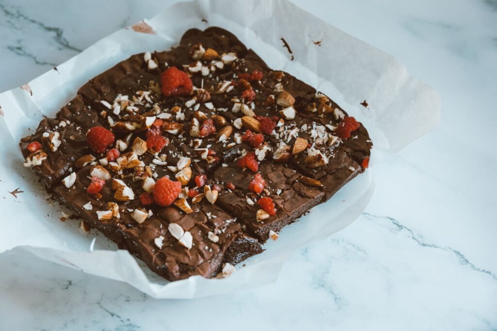 Freshly baked chocolate brownie topped with almonds and raspberries on parchment paper