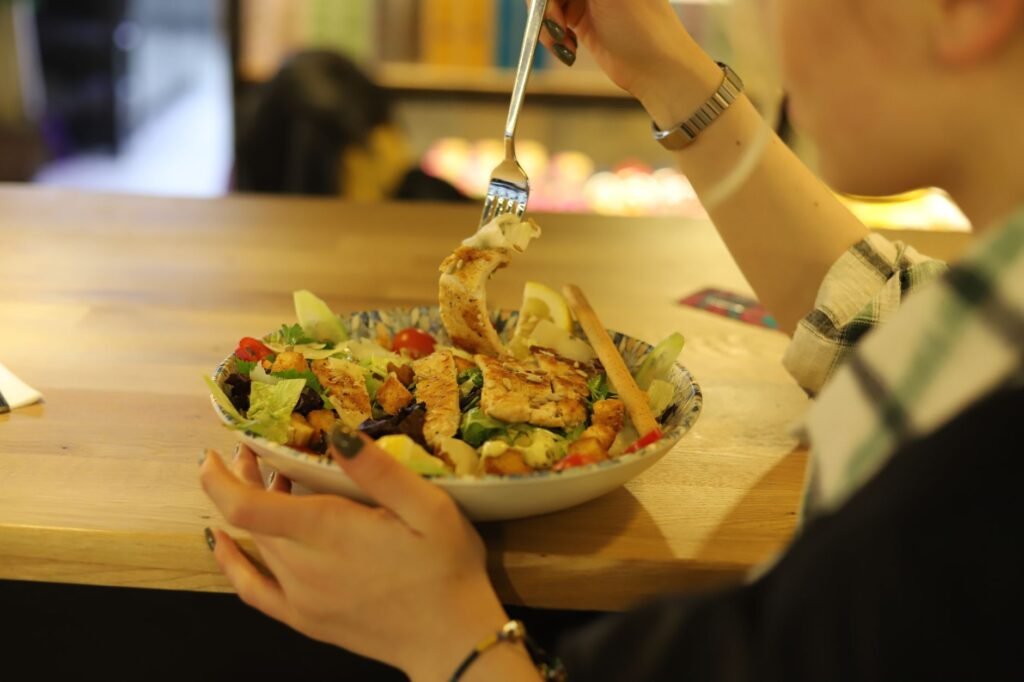 Close-up of a person enjoying a fresh chicken salad at a wooden table indoors