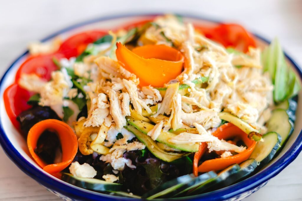 A vibrant salad with shredded chicken, fresh vegetables, and colorful toppings in a bowl.