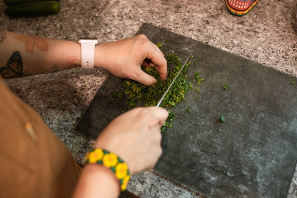 Hands chopping fresh cilantro on a cutting board, showcasing food preparation.