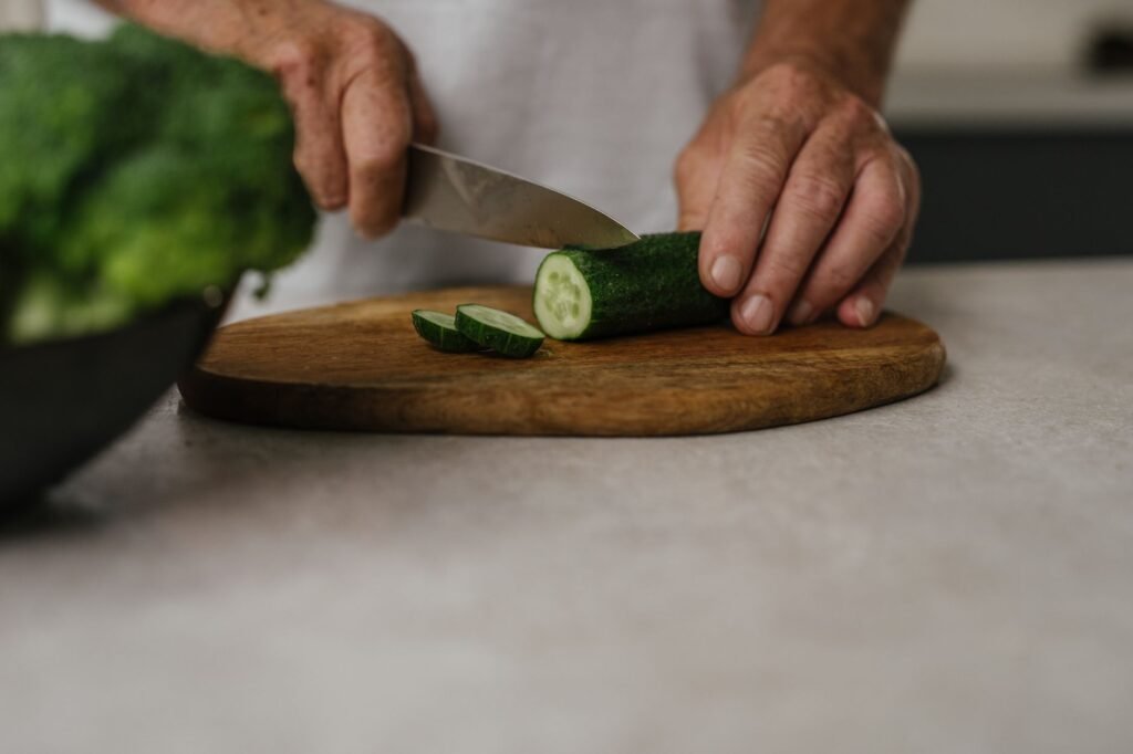 Close-up of hands slicing cucumber on wooden board in kitchen setting