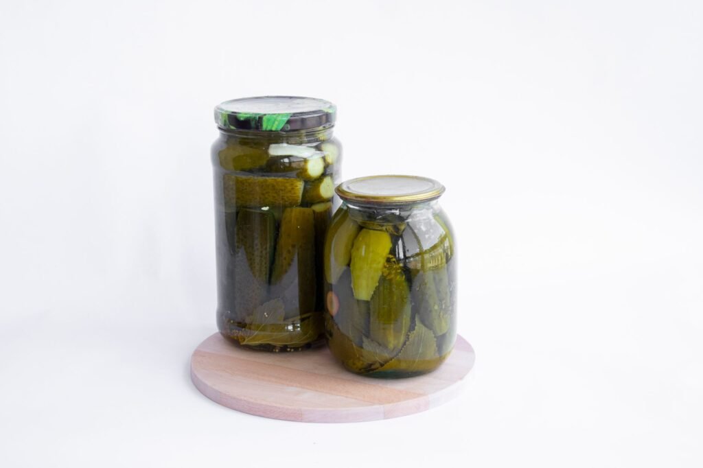 Two jars of pickles sit on a wooden board, showcasing preserved cucumbers in a still life composition