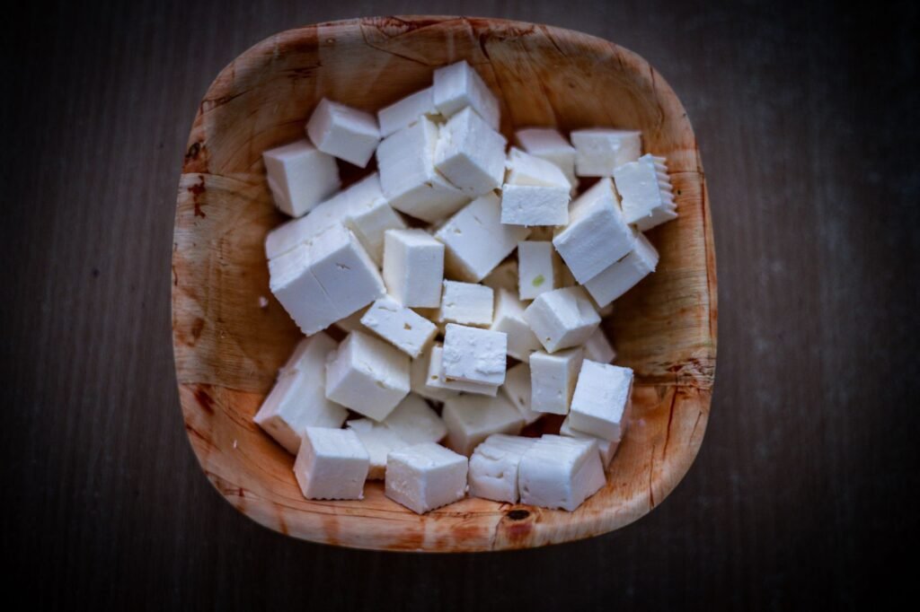 Top view of fresh feta cheese cubes in a rustic wooden bowl, showcasing clean and minimal food photography