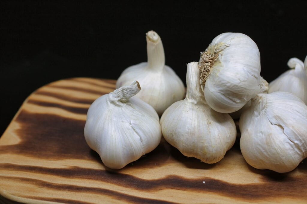 Fresh garlic bulbs placed on a wooden board with a black background, perfect for culinary themes