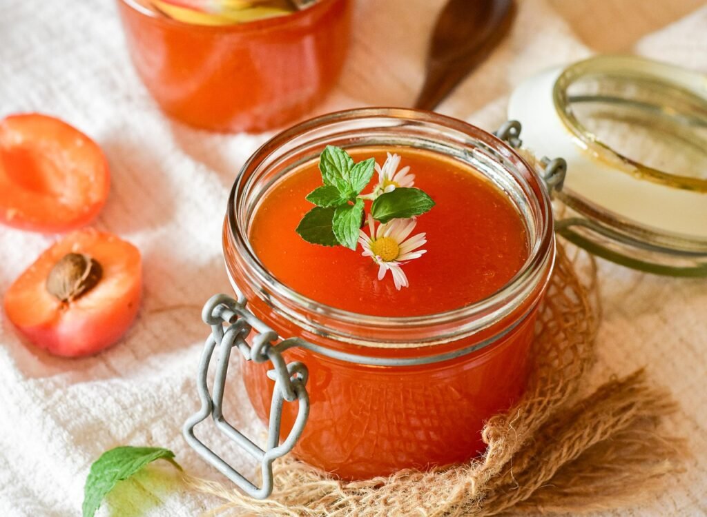 Glass jar of apricot jam with a clamp lid beside halved apricots on a white cloth