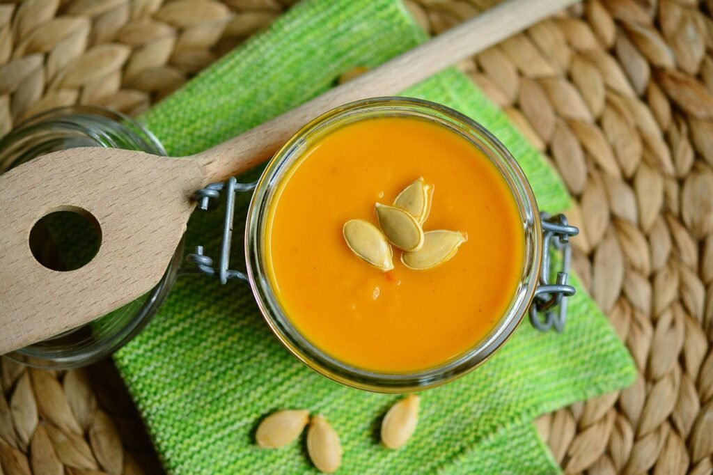 Glass jar with a clamp lid filled with orange pumpkin soup topped with seeds on a green napkin