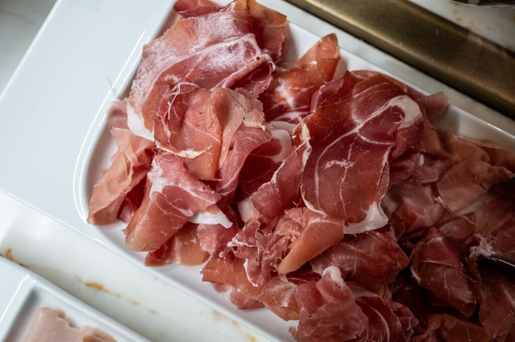 Freshly sliced prosciutto ham served on a white tray in the kitchen.
