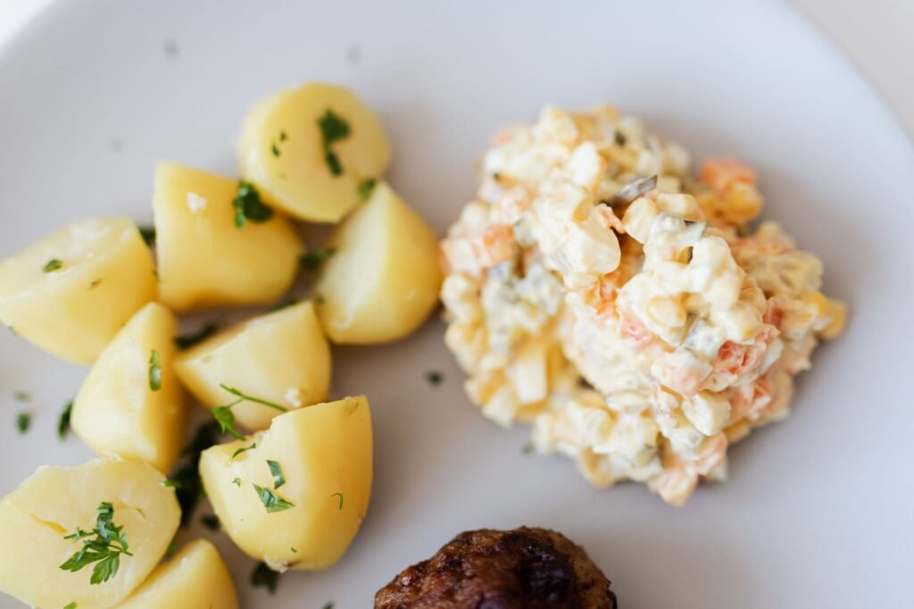 From above plate with boiled potatoes with parsley and portion of tasty nutritious Russian salad with boile...