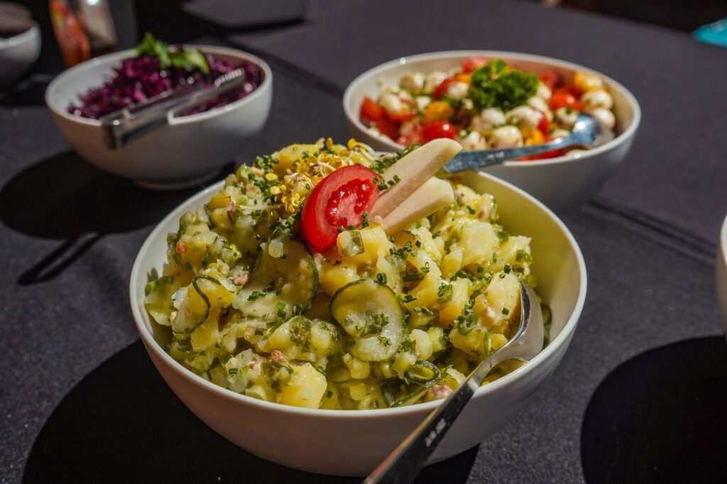 A close-up of vibrant potato salad garnished with fresh herbs, served outdoors on a sunny day.