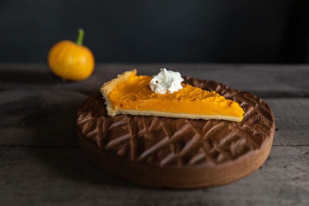 A close-up of a pumpkin pie slice topped with whipped cream, perfect for fall desserts