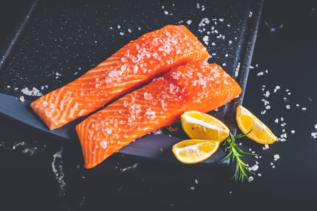 Close-up of raw salmon fillets garnished with salt, lemon wedges, and rosemary on a baking tray