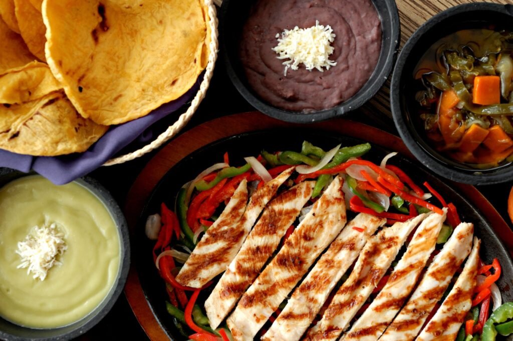 Top view of grilled chicken fajitas with tortillas, beans, and sauces, showcasing a vibrant Mexican meal