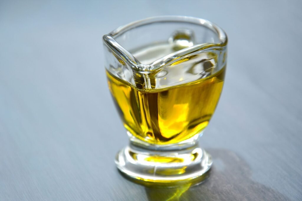 Small glass pitcher filled with clear yellow cooking oil on a gray table