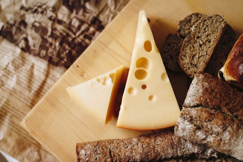 Wedges of pale yellow cheese with large round holes on a board with dark bread
