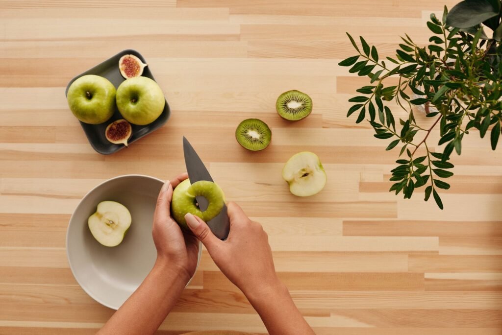 Hands peeling green apples with kiwi and figs, fresh and healthy food setup