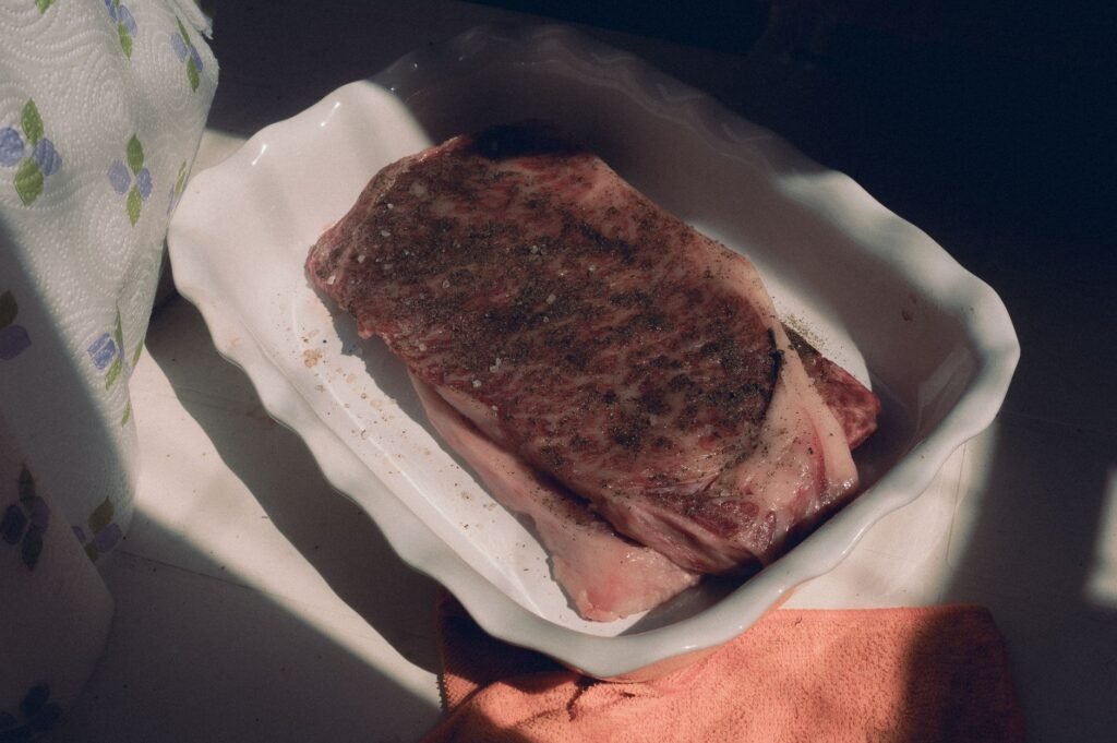 Marbled raw beef steak seasoned and ready in a baking dish, capturing natural light