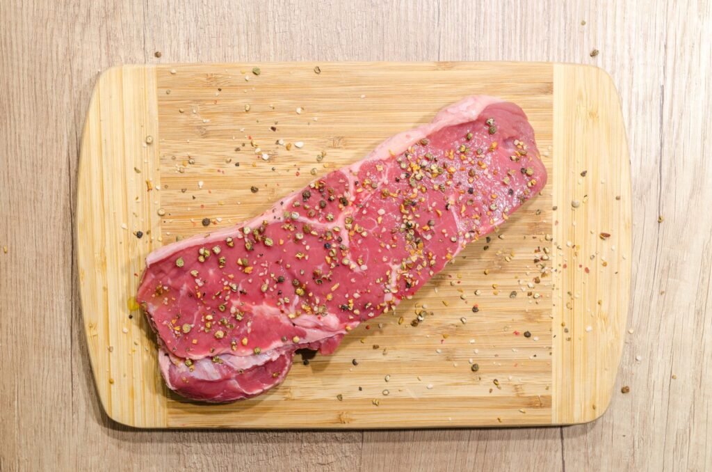 Raw beef steak seasoned with spices on a wooden chopping board. Perfect for cooking enthusiasts