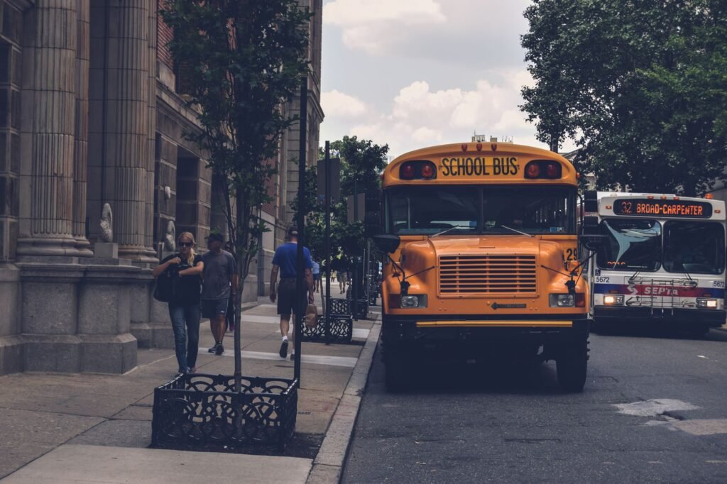 A school bus parked on a city street with pedestrians and a SEPTA bus in Philadelphia.
