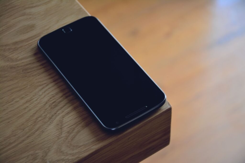 A smartphone sits quietly on the edge of a wooden table, displaying modern technology's sleek design