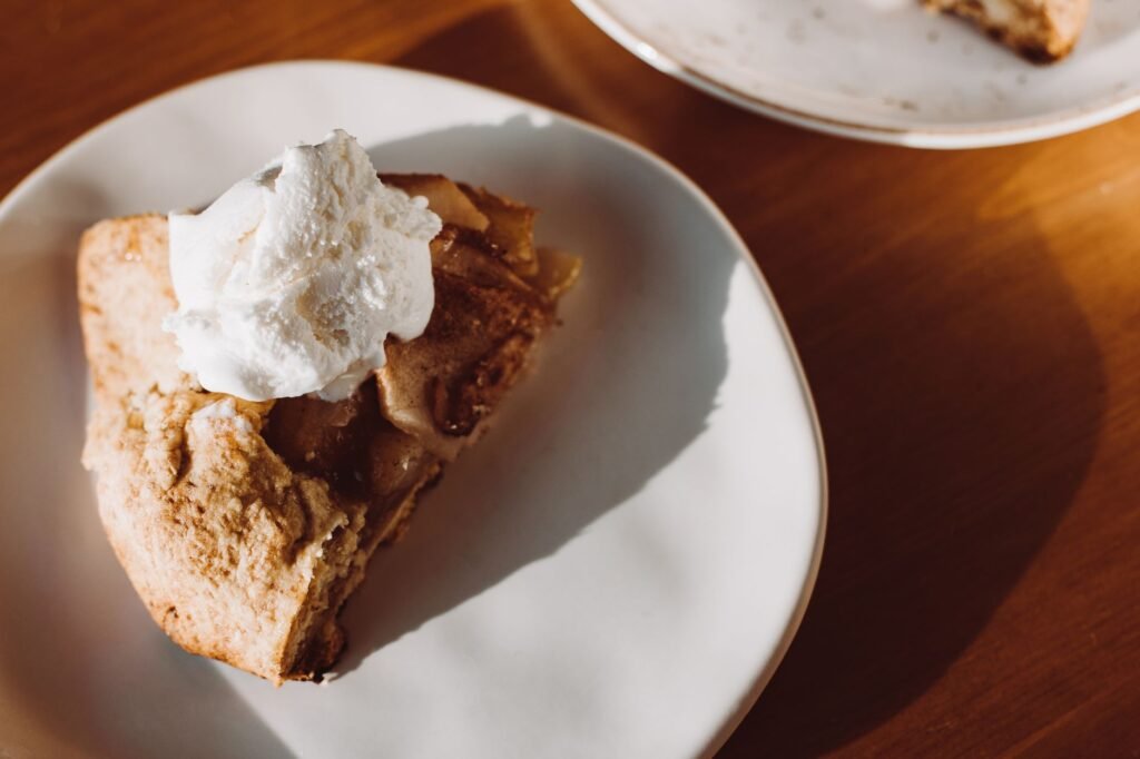 Close-up of a slice of homemade apple pie topped with whipped cream on a ceramic plate