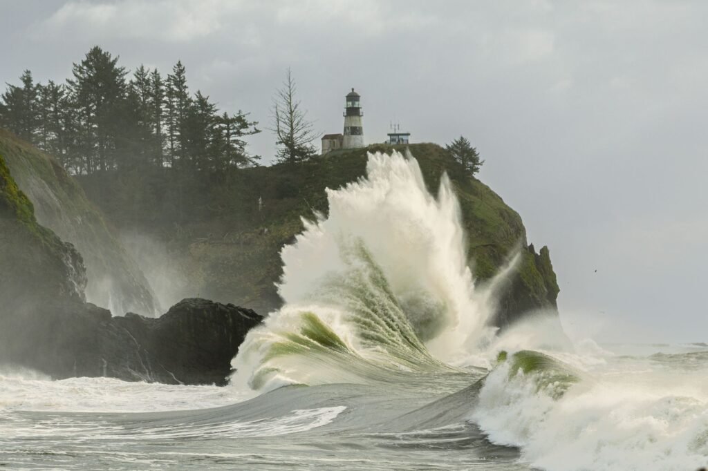 Powerful ocean waves crash against the rocky cliffs at Cape Disappointment with lighthouse view