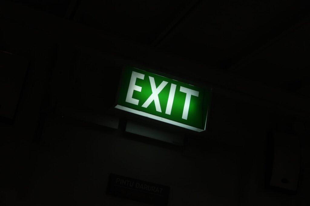 Glowing green exit sign mounted high on a wall in a dark corridor