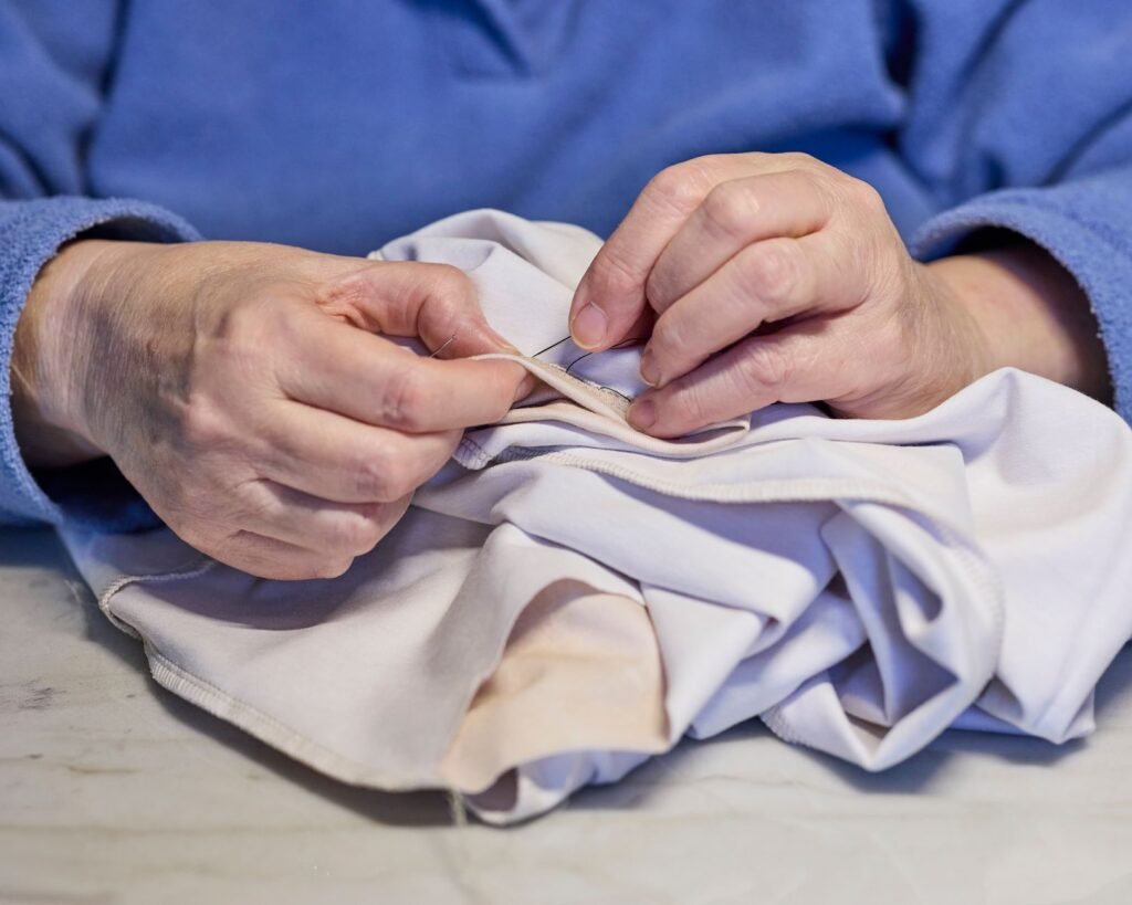 Two hands stitching a tear in a white cloth garment on a table