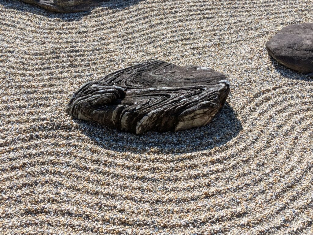 Raked gravel with swirling lines around a dark flat stone in a dry garden
