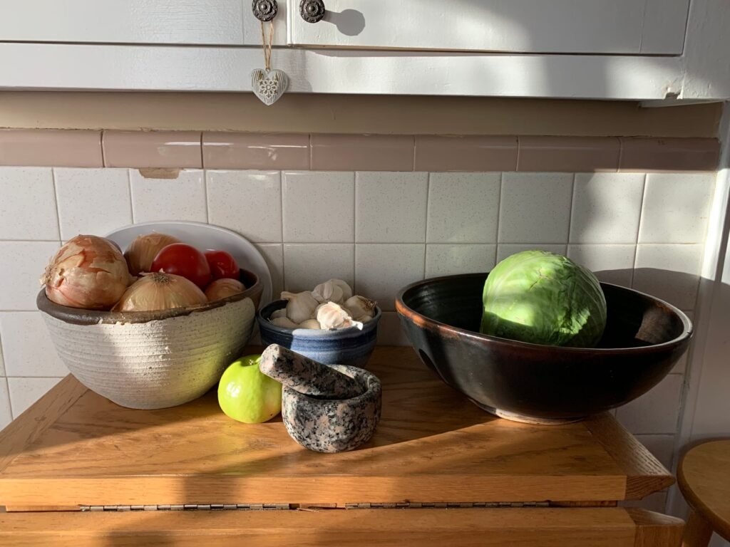 Assorted fresh vegetables on a wooden kitchen counter with natural sunlight