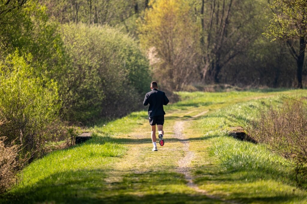 A man jogs on a scenic, grassy forest path surrounded by lush greenery under daylight