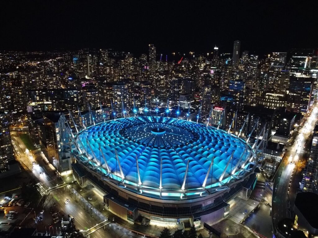 Domed stadium roof glowing blue at night surrounded by city lights and towers