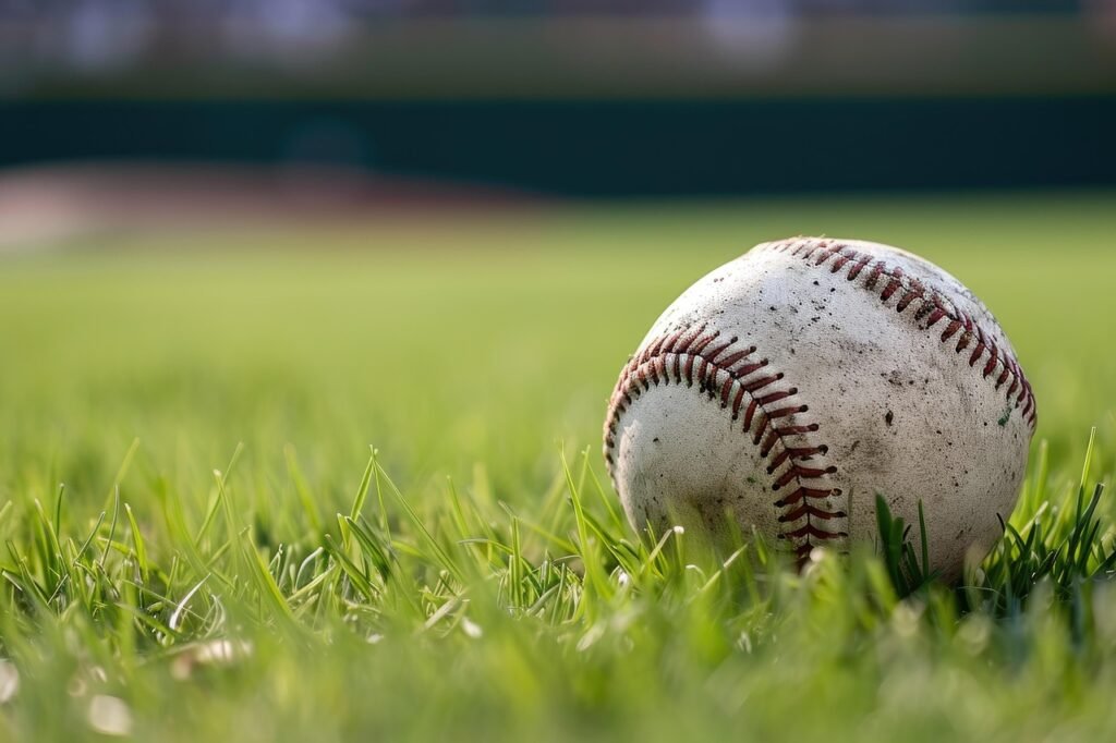 Worn white baseball with red stitching resting in short green grass