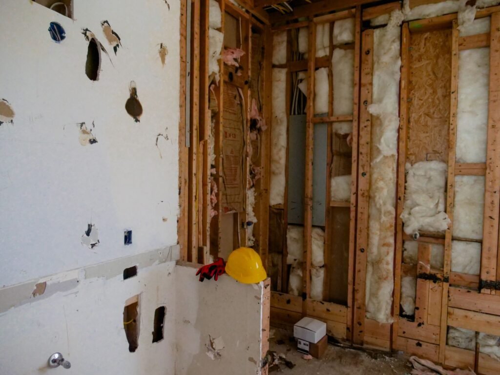 Gutted room with bare wood stud walls, insulation, debris and a yellow hard hat