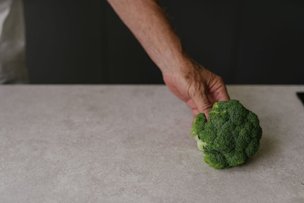 Close-up of a senior's hand holding fresh green broccoli on a light table surface