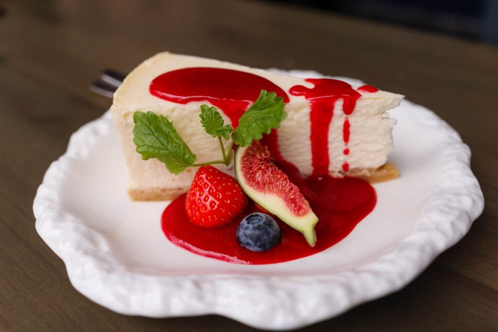 Creamy cheesecake with berries and fig on a white plate. Topped with red fruit sauce