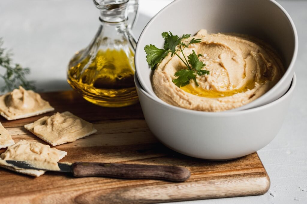 Close-up of a bowl of creamy hummus topped with olive oil and herbs, accompanied by crackers