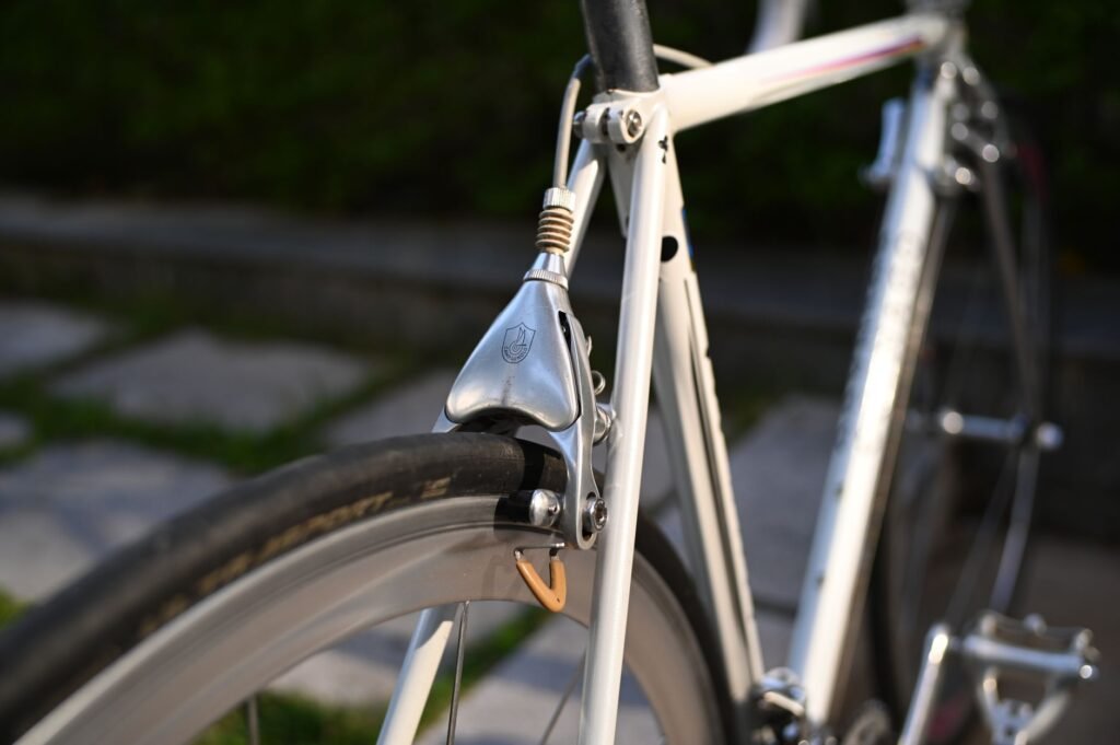 Silver caliper rim brake mounted over the tire of a light gray road bicycle