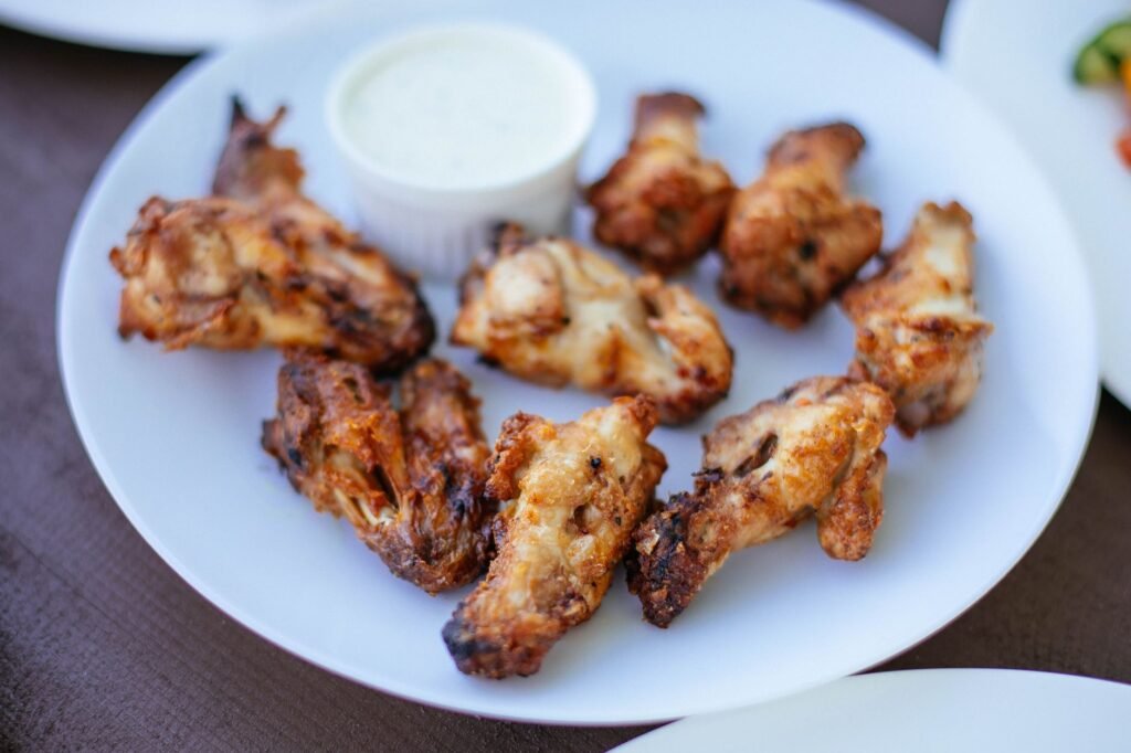 Plate of crispy browned chicken wings served with a small cup of white dipping sauce