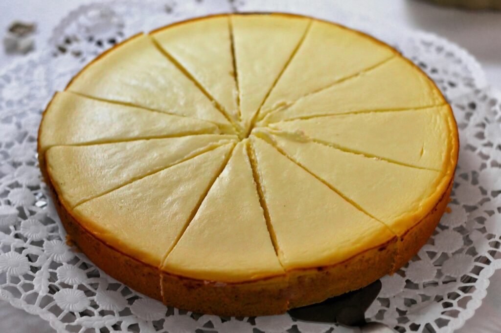 Whole golden baked cheesecake scored into wedges on a white lace doily